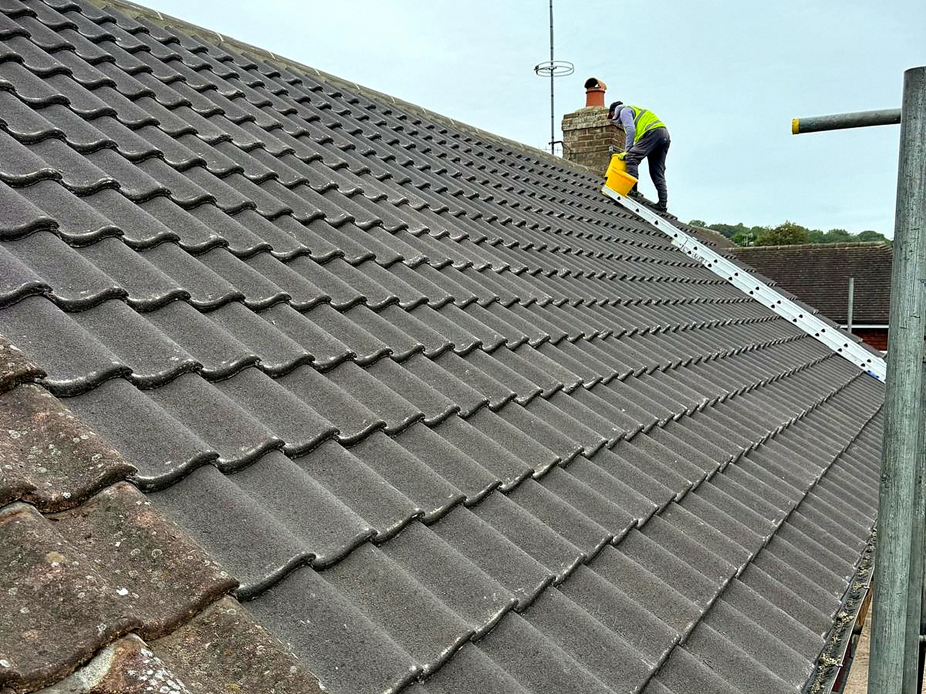 Finished roof in new interlocking tiles with a roofer bedding the ridge
