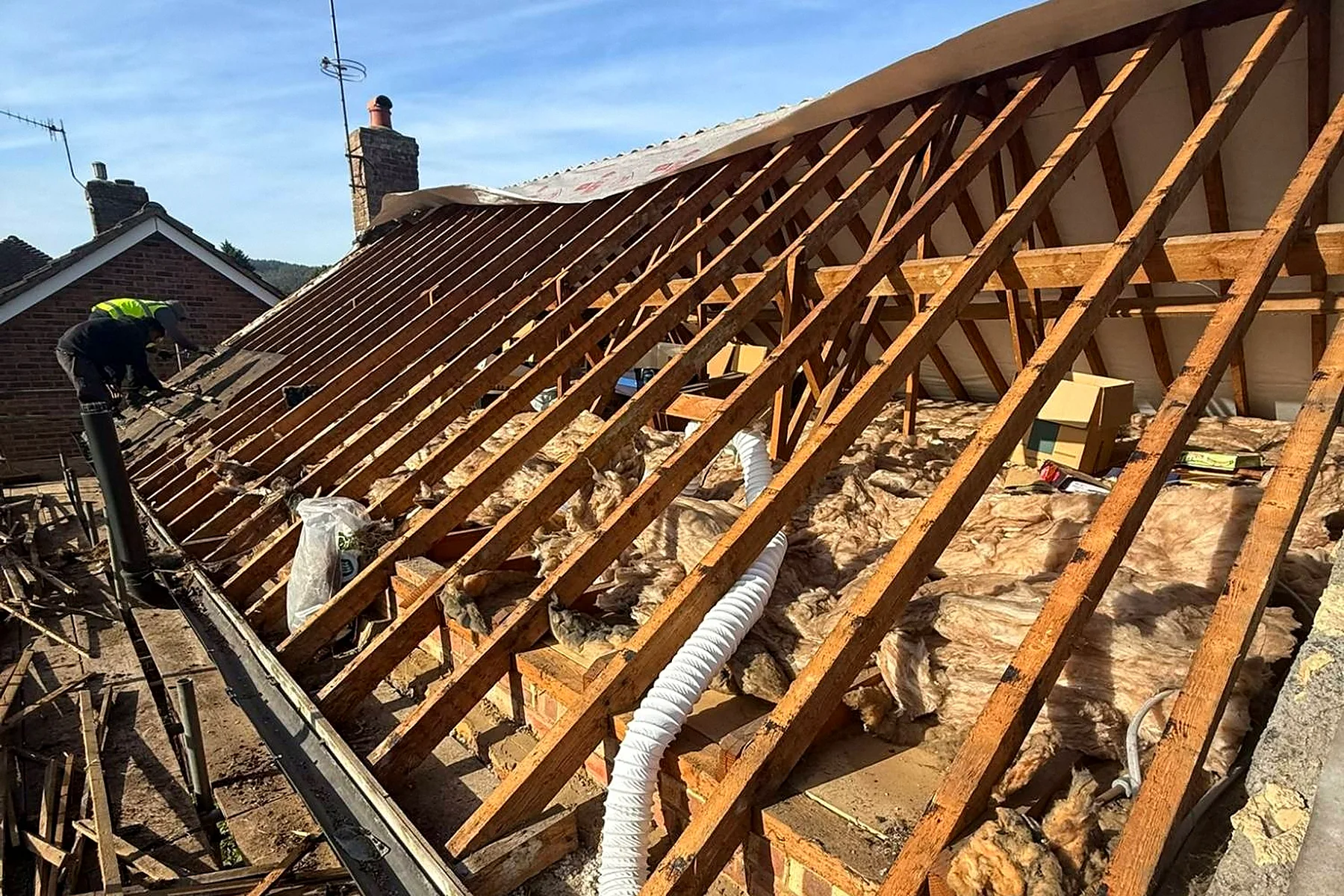 The roof open to the rafters with the old battens away and the loft insulation visible