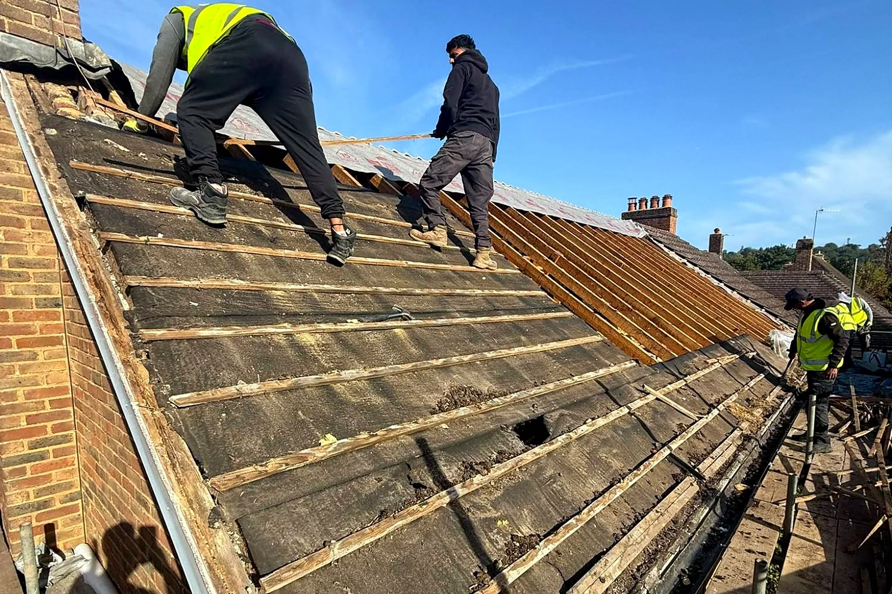 Roofers stripping the old tiles and battens off the roof in sections