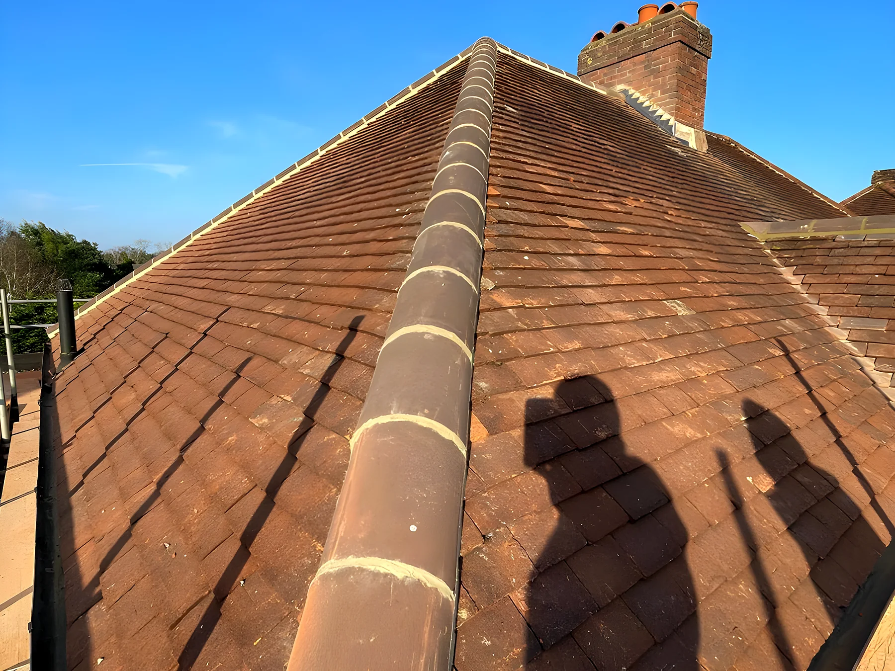 A hipped clay tile roof with bonnet hips under a blue sky