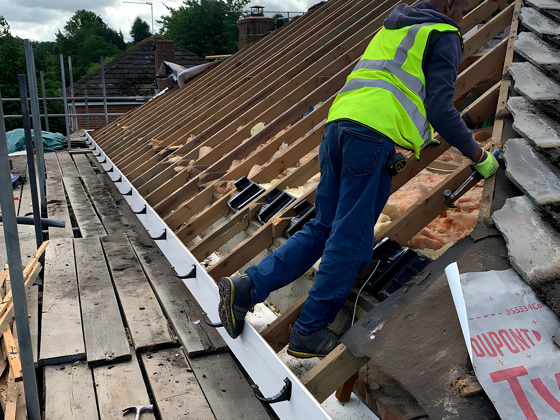 Roofer working along a roof slope during a repair, ladder and safety edge in place