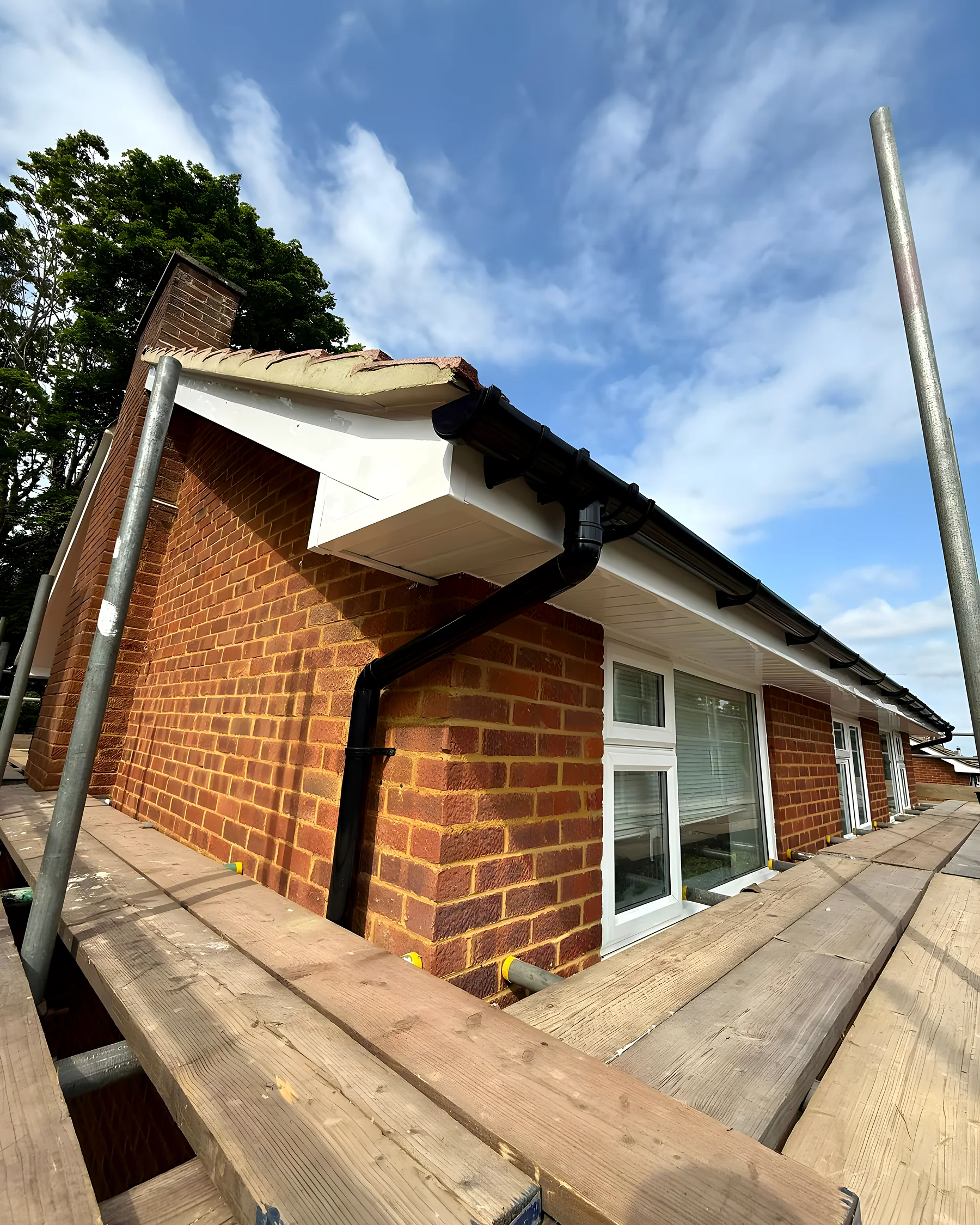 Roofer on a ladder fitting new white uPVC fascia and guttering to a brick house