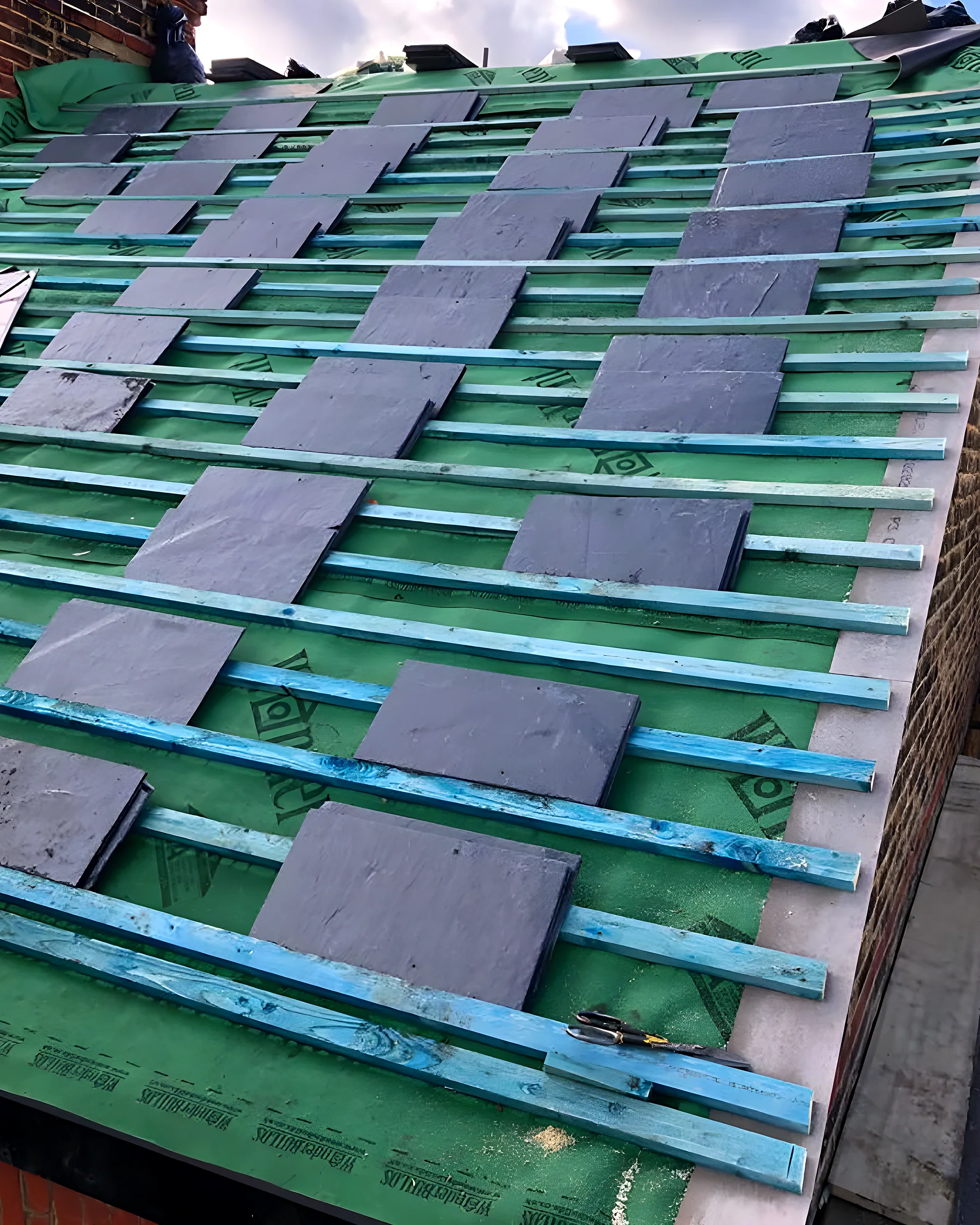 New battens and underlay across a stripped roof with slates being loaded out