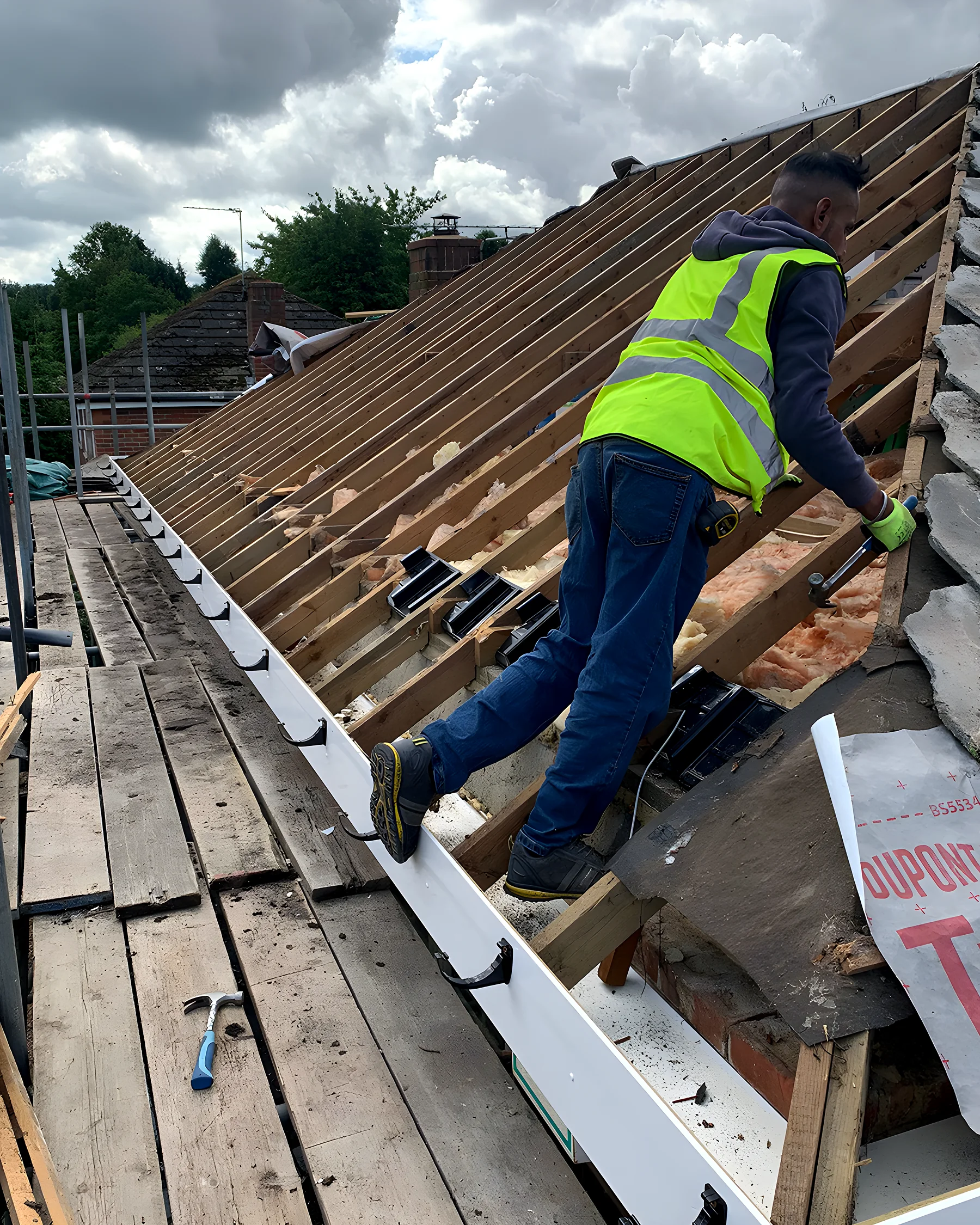 Roofer working along a roof slope during a repair, ladder and safety edge in place