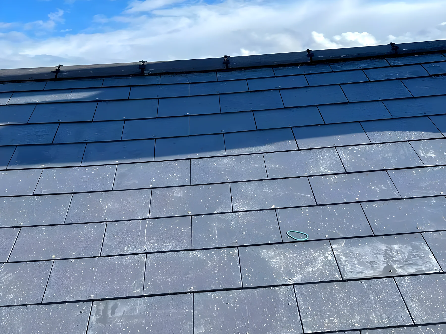 Blue grey slate roof photographed from the scaffold against a bright sky